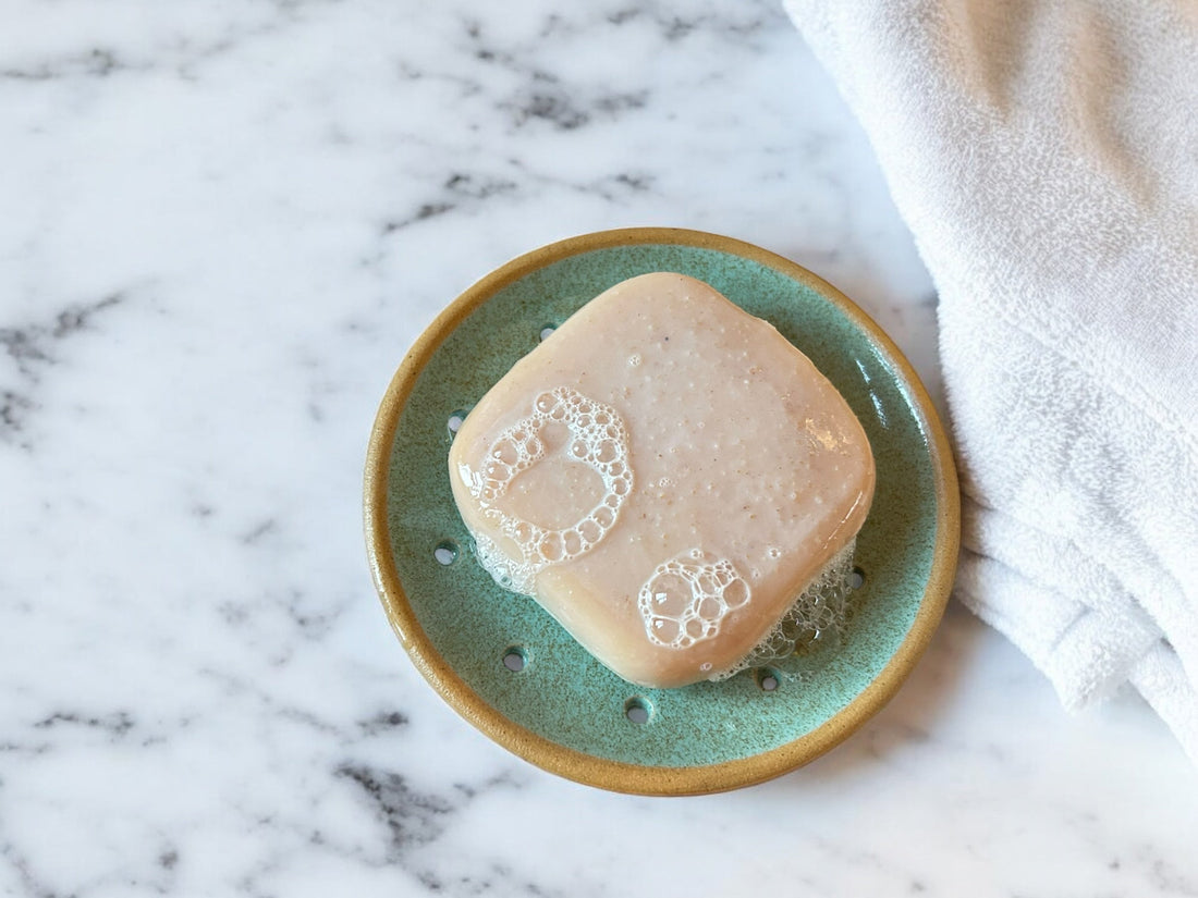 Cremefarbene Naturseife mit frischem Schaum auf einer türkis glasierten Keramik-Seifenablage mit Abflusslöchern