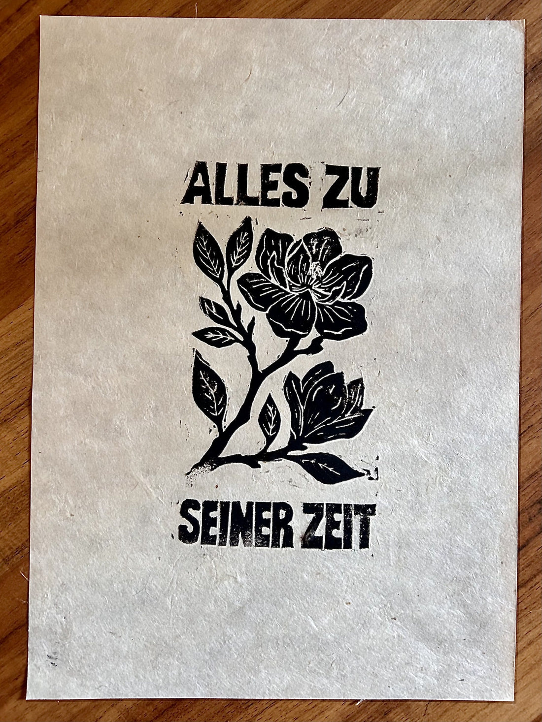 Handabzug eines Linolschnitts auf Lokta-Papier: eine Magnolienblüte mit dem Schriftzug „Alles zu seiner Zeit“ in Schwarz